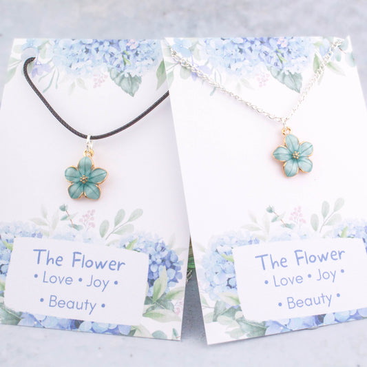 A blue flower necklace available on either a chain or cord. It comes backed onto a card with the symbolic meanings of a flower. "Love, Joy and Beauty"
