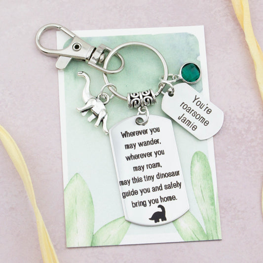 This shows the fully personalised travel Dinosaur keyring which includes the silver Dinosaur charm, the engraved quote tag which reads: “Wherever you may wander, wherever you may roam, may this tiny Dinosaur guide you and bring you safely home” a birthstone and a mini engraved gift message tag. It also has a clasp to attach to a bag.