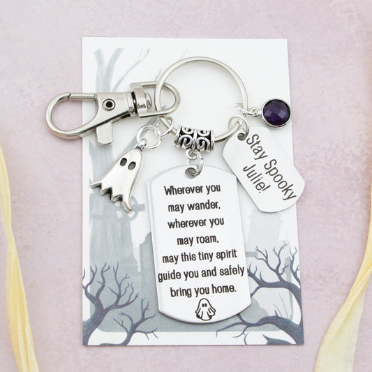 A keyring with two charms on a matching backing card. The charms are a silver Ghost and a quote charm that reads “Wherever you may wander, wherever you may roam, may this tiny Ghost guide you and bring you safely home”