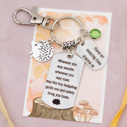 This shows the fully personalised travel hedgehog keyring which includes the silver hedgehog charm, the engraved quote tag which reads: “Wherever you may wander, wherever you may roam, may this tiny hedgehog guide you and bring you safely home” a birthstone and a mini engraved gift message tag. It also has a clasp to attach to a bag.