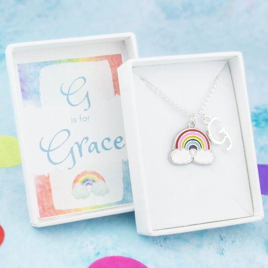 A silver chain necklace with a rainbow pendant and initial charm. The gift box is personalised with the name of the recipient.