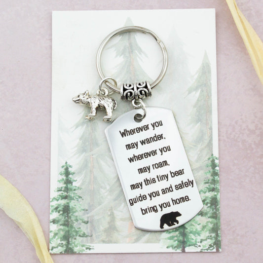 A keyring with two charms on a matching backing card. The charms are a silver Bear and a quote charm that reads “Wherever you may wander, wherever you may roam, may this tiny Bear guide you and bring you safely home”