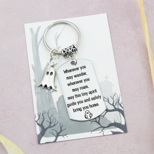 A keyring with two charms on a matching backing card. The charms are a silver Ghost and a quote charm that reads “Wherever you may wander, wherever you may roam, may this tiny spirit guide you and bring you safely home”