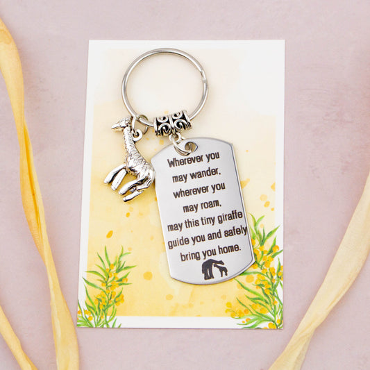A keyring with two charms on a matching backing card. The charms are a silver giraffe and a quote charm that reads “Wherever you may wander, wherever you may roam, may this tiny giraffe guide you and bring you safely home”
