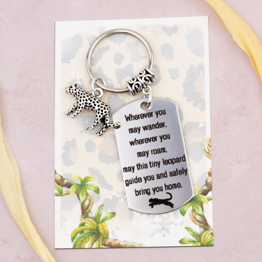 A keyring with two charms on a matching backing card. The charms are a silver leopard and a quote charm that reads “Wherever you may wander, wherever you may roam, may this tiny leopard guide you and bring you safely home”