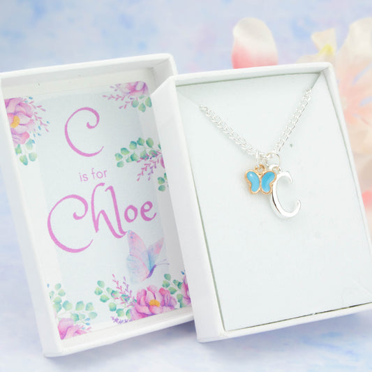 A silver chain necklace with a blue butterfly pendant and initial charm. The gift box is personalised with the name of the recipient.