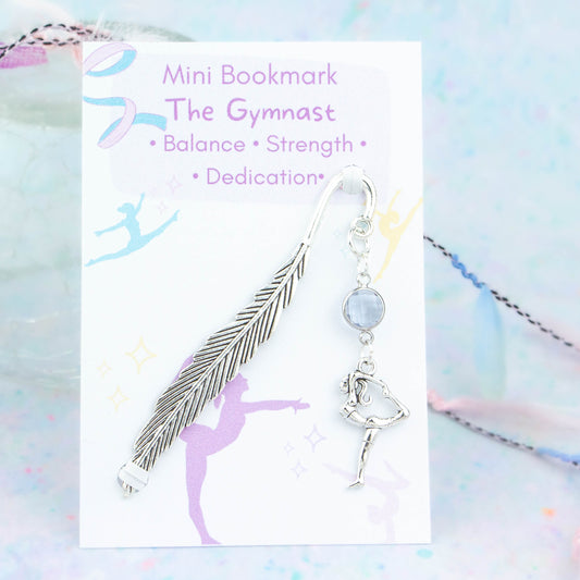 A gymnast charm hanging from a metal bookmark. It has a light purple crystal. The bookmark is backed onto a card with what the charm means symbolically.