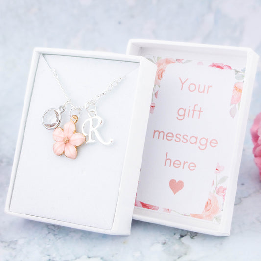 A pink flower necklace personalised with an initial and birthstone. It's on a silver chain. The gift box lid can be personalised with your message.