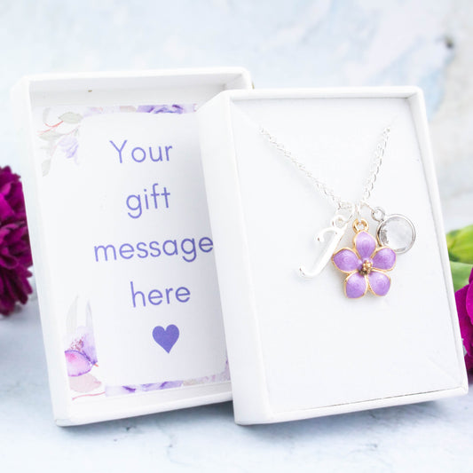 A purple flower necklace personalised with an initial and birthstone. It's on a silver chain. The gift box lid can be personalised with your message.