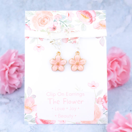 A pair of pink flower clip on earrings. It's backed onto a card that says the symbolic meanings of the flower - love, joy and beauty.