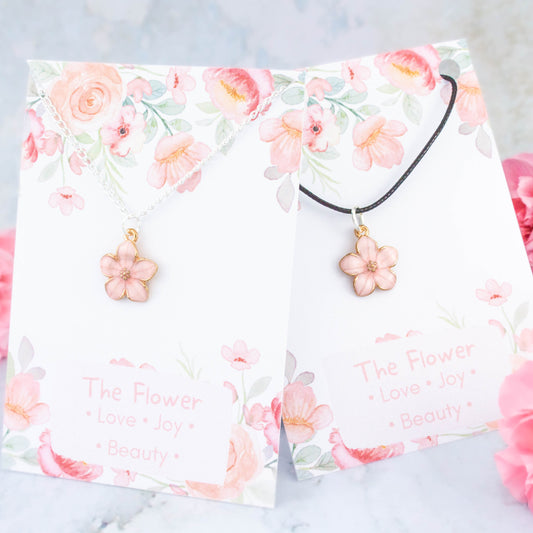 A pink flower necklace available on either a chain or cord. It comes backed onto a card with the symbolic meanings of a flower. "Love, Joy and Beauty"