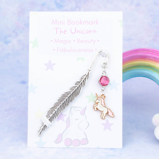 A pink unicorn charm hanging from a metal bookmark. It has a pink crystal. The bookmark is backed onto a card with what the charm means symbolically.