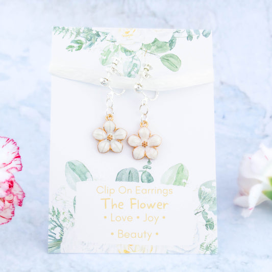 A pair of white flower clip on earrings. It's backed onto a card that says the symbolic meanings of the flower - love, joy and beauty.