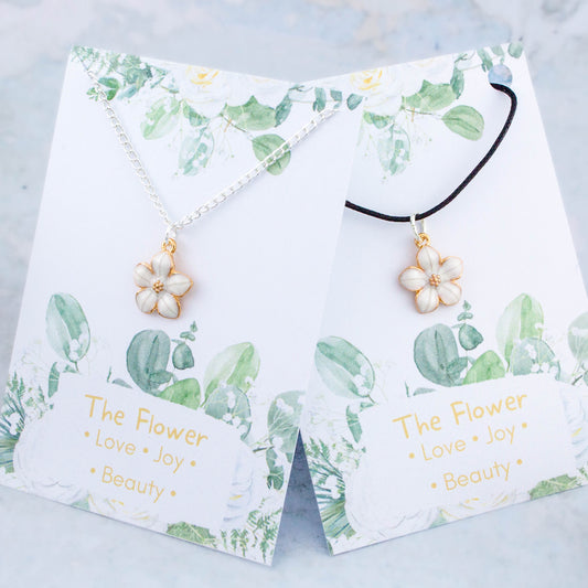 A white flower necklace available on either a chain or cord. It comes backed onto a card with the symbolic meanings of a flower. "Love, Joy and Beauty"