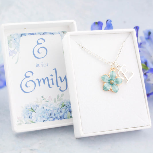 A blue flower and initial charm silver chain necklace. It comes in a white personalised gift box with the recipients name printed inside the lid.