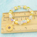 A silver and yellow sunflower charm bracelet against a ruler. 