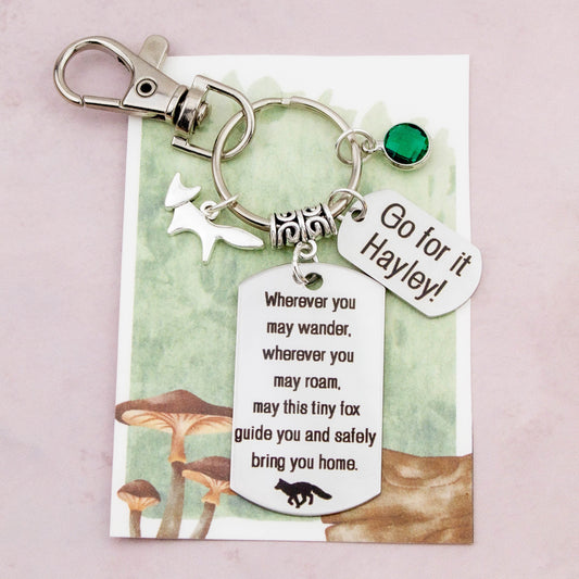 This shows the fully personalised travel fox keyring which includes the silver fox charm, the engraved quote tag which reads: “Wherever you may wander, wherever you may roam, may this tiny fox guide you and bring you safely home” a birthstone and a mini engraved gift message tag. It also has a clasp to attach to a bag. 