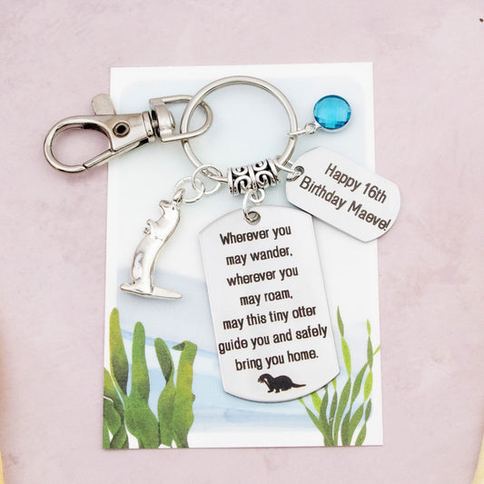 This shows the fully personalised travel otter keyring which includes the silver otter charm, the engraved quote tag which reads: “Wherever you may wander, wherever you may roam, may this tiny otter guide you and bring you safely home” a birthstone and a mini engraved gift message tag. It also has a clasp to attach to a bag. 