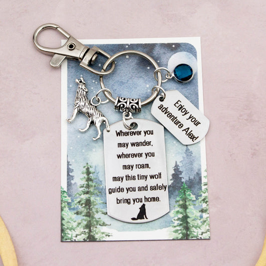 This shows the fully personalised travel wolf keyring which includes the silver wolf charm, the engraved quote tag which reads: “Wherever you may wander, wherever you may roam, may this tiny wolf guide you and bring you safely home” a birthstone and a mini engraved gift message tag. It also has a clasp to attach to a bag. 