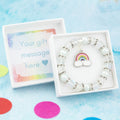 An enamel rainbow charm bracelet made with white beads. It is in a personalised gift box.