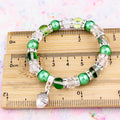 A silver and green acorn charm bracelet against a ruler. 