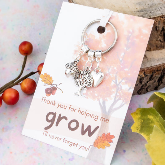 A keyring with an acorn, a tree and a heart charm. The backing card reads "Thank you for helping me grow. I'll never forget you!"