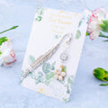 A metal charm bookmark with a dangling white flower and crystal charm.