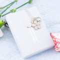 The white flower necklace with initial and birthstone shown against the gift box lid. The top of the lid has our logo on it in silver foil.