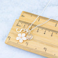 A white flower necklace with initial and birthstone shown against a ruler for measurements.