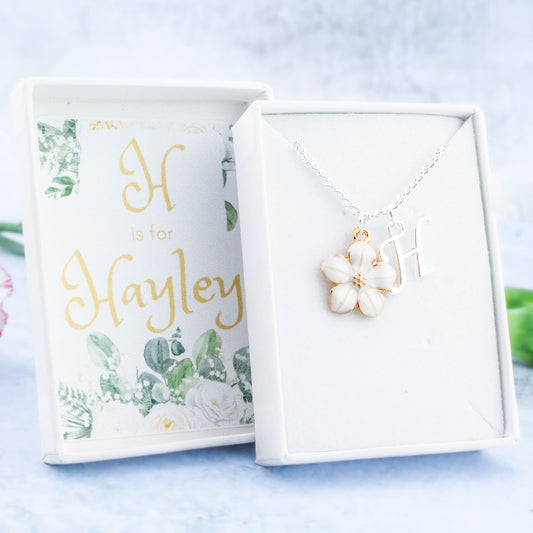A white flower and initial charm silver chain necklace. It comes in a white personalised gift box with the recipients name printed inside the lid.