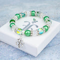 A silver and green four leaf clover charm bracelet against a ruler. 