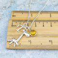 A personalised giraffe charm necklace against a ruler. 