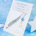 A gold star charm on a metal bookmark in the shape of a feather. It is backed onto a card with the symbolic meanings of the charm. 