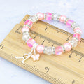 A silver and pink butterfly charm bracelet against a ruler. 