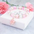 The pink flower girl bracelet sitting on the gift box, it shows the foiled silver logo on the lid.