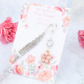 A metal charm bookmark with a dangling pink flower and crystal charm.