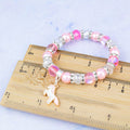 A silver and pink unicorn charm bracelet against a ruler.