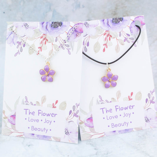 A purple flower necklace available on either a chain or cord. It comes backed onto a card with the symbolic meanings of a flower. "Love, Joy and Beauty"