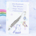A purple unicorn charm hanging from a metal bookmark. It has a purplecrystal. The bookmark is backed onto a card with what the charm means symbolically.  