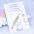 An enamel purple unicorn charm on a metal bookmark in the shape of a feather. It is backed onto a card with the symbolic meanings of the charm. 