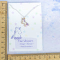 A purple unicorn charm necklace against a ruler. 