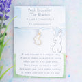 A white rabbit wish bracelet backed on a card with a poem about wish bracelets and the symbolism of a rabbit.